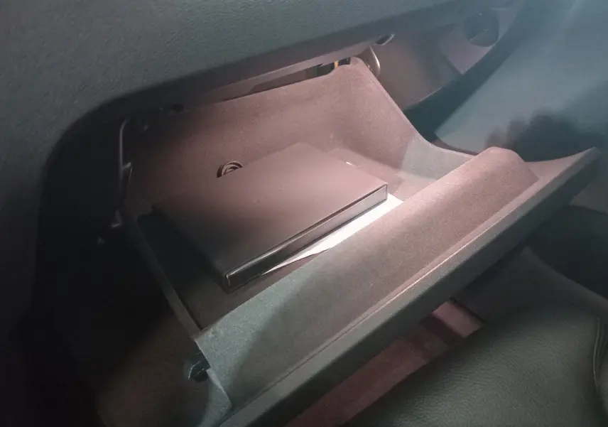 Gant de rangement ouvert côté passager du Volvo XC60 gris clair, montrant un boîtier noir à l'intérieur.