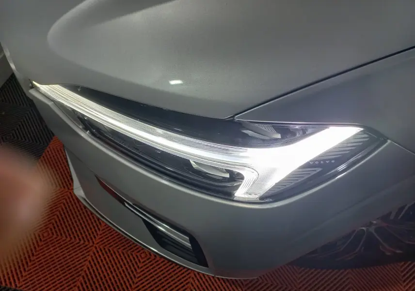 Gros plan sur le phare avant droit allumé du Volvo XC60 gris clair, soulignant son design LED distinctif.