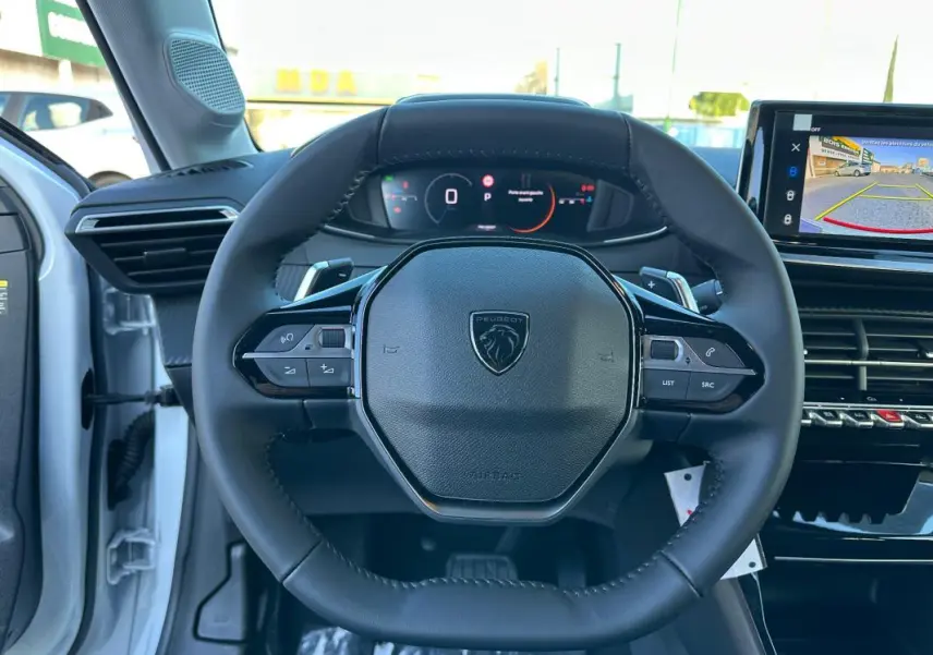 Vue intérieure centrée sur le volant cuir noir de la Peugeot 208 Hybrid 110 blanc avec cockpit numérique et écran tactile.