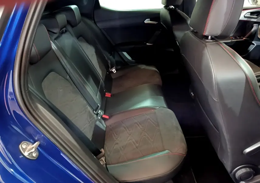 Vue intérieure côté gauche des sièges arrière en cuir noir avec surpiqûres rouges d'une SEAT Leon bleu 2021.