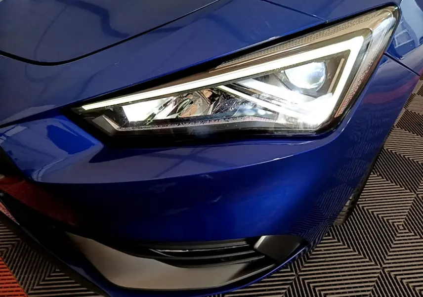 Gros plan sur le phare avant droit allumé d’une SEAT LEON bleu électrique, soulignant ses lignes anguleuses modernes.