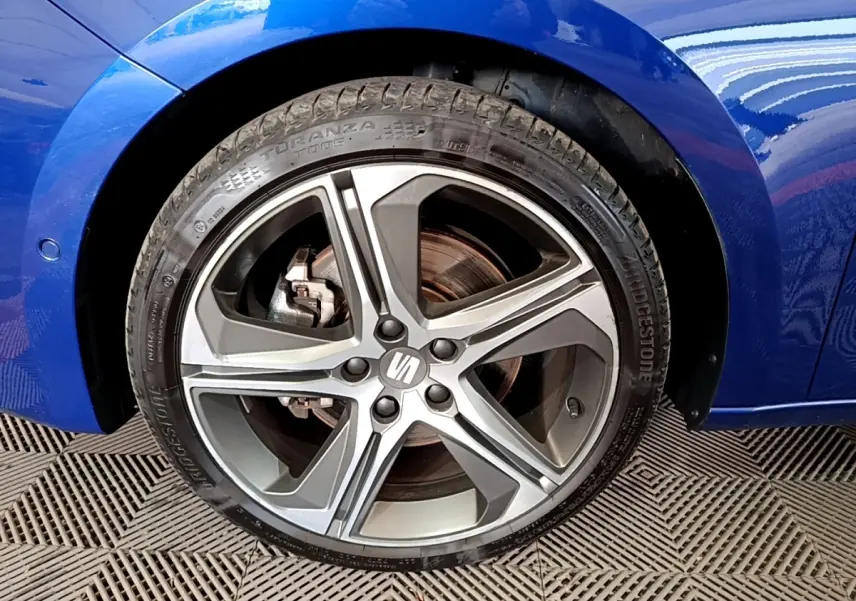 Gros plan sur la roue avant gauche d'une SEAT Leon bleu 2021, mettant en valeur l'aile et le pneu Bridgestone.