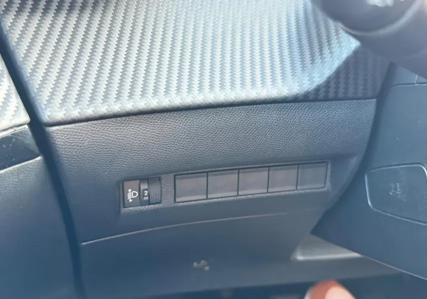 Détail intérieur montrant la console côté conducteur avec finition carbone et commandes d’éclairage du Peugeot 2008 noir.