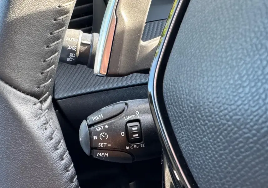 Gros plan sur la commande de régulateur de vitesse au volant d’un Peugeot 2008 noir Hybrid 136 e-DCS6 Allure.