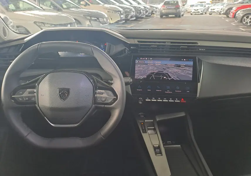 Vue intérieure du poste de conduite de la Peugeot 308 2023 avec volant compact et écran tactile central affichant la navigation.
