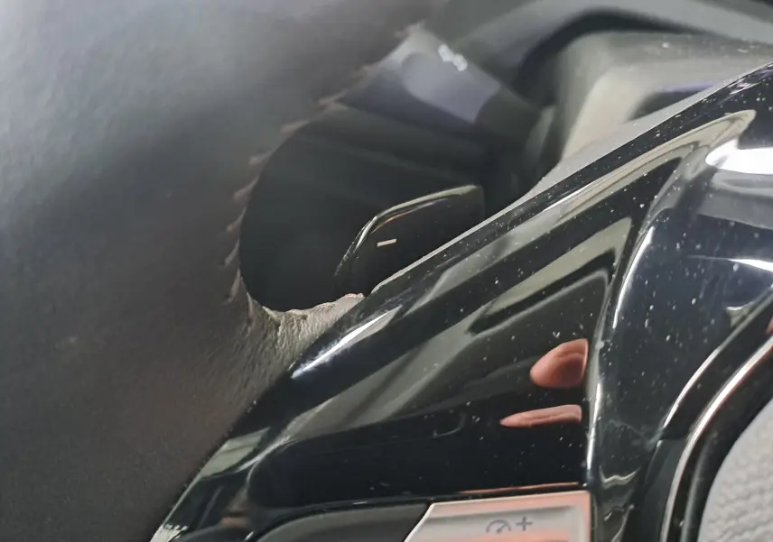 Gros plan sur la commande de régulateur de vitesse au volant noir brillant d'une Peugeot 308 gris Artense 2023.