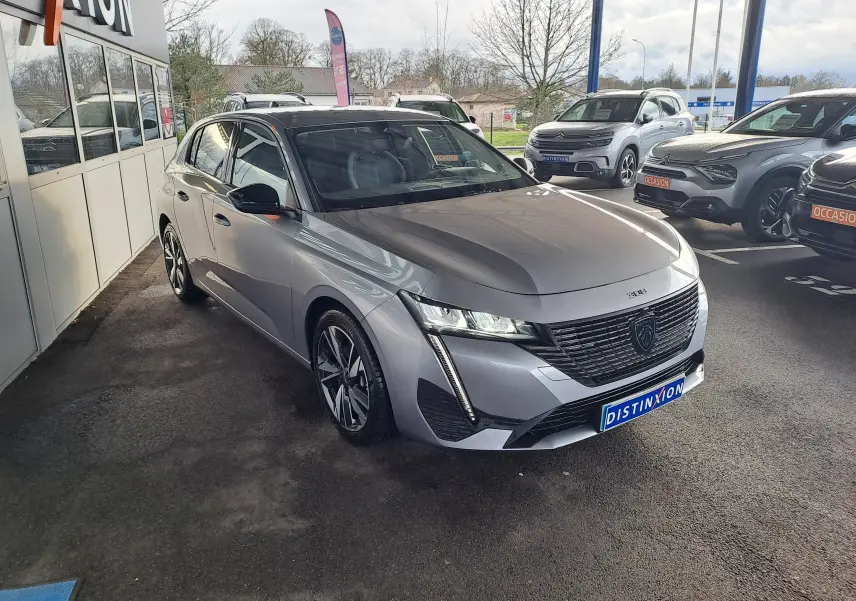 Peugeot 308 Gris Artense vue 3/4 avant droit, avec calandre noire distinctive et feux LED fins.