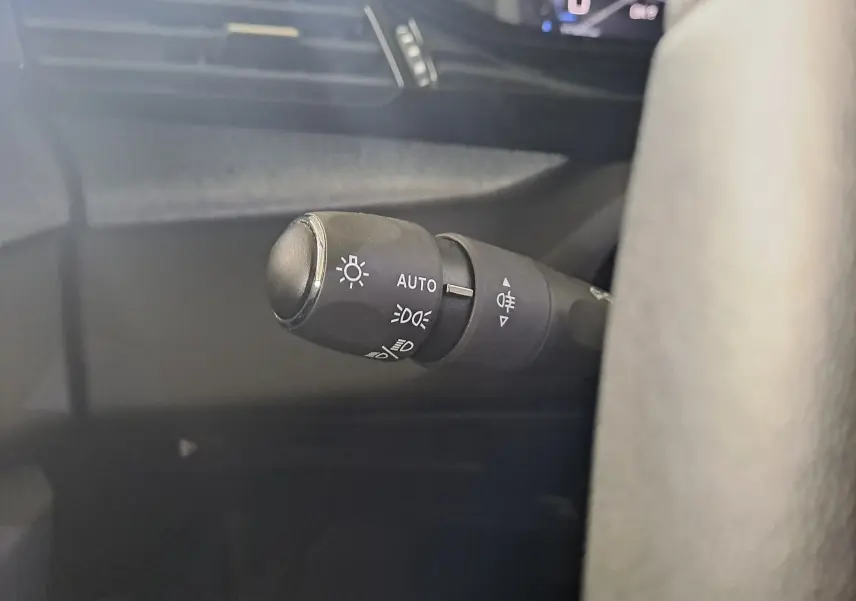 Gros plan sur la commande des feux automatiques à gauche du volant dans l'habitacle d'une Peugeot 308 gris Artense 2023.