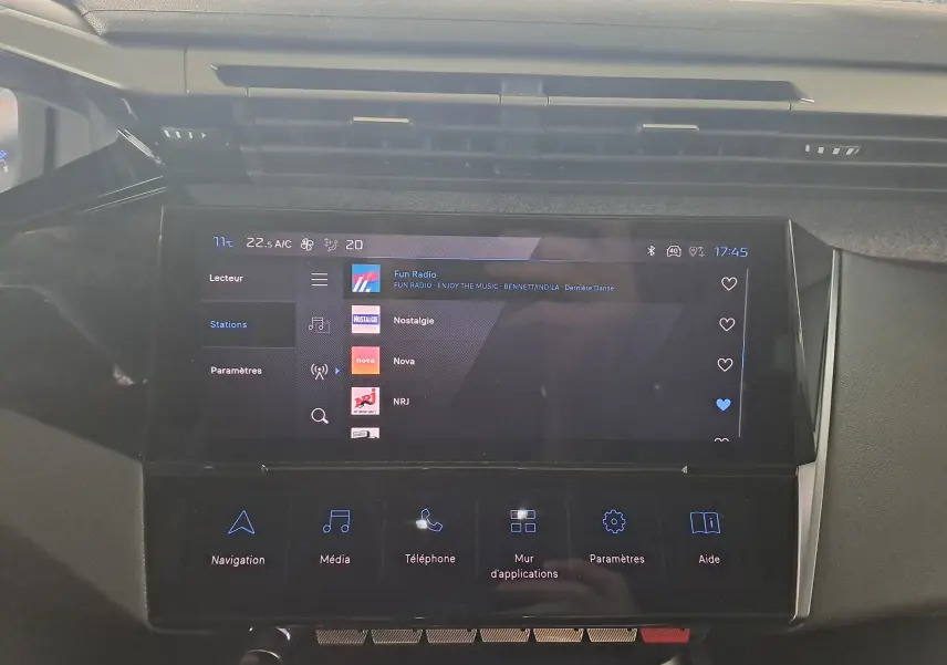 Écran tactile central du tableau de bord de la Peugeot 308 gris Artense, affichant les stations radio et options multimédia.
