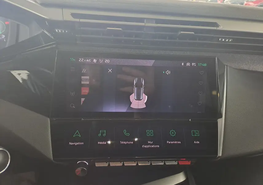 Écran tactile central du tableau de bord de la Peugeot 308 2023, affichant l'aide au stationnement et les options multimédia.