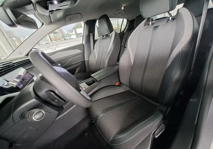 Intérieur de la Peugeot 308 2023, vue côté conducteur, sièges gris avec surpiqûres bleues et tableau de bord moderne.