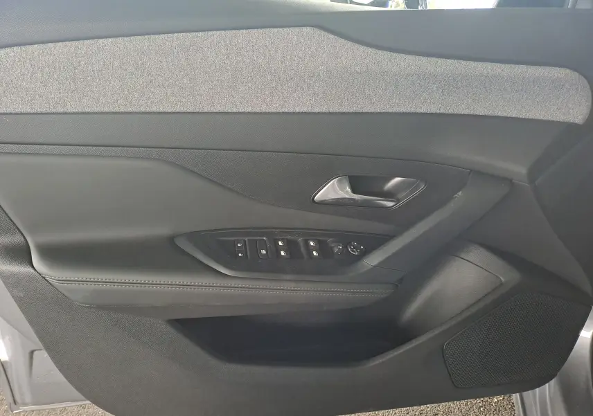 Intérieur côté gauche de la porte avant d'une Peugeot 308 gris Artense, avec commandes électriques et garniture tissu.