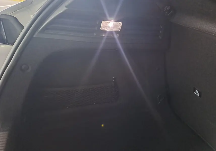 Intérieur du coffre noir d'une Peugeot 308 gris Artense, avec filet de rangement et éclairage allumé côté gauche.