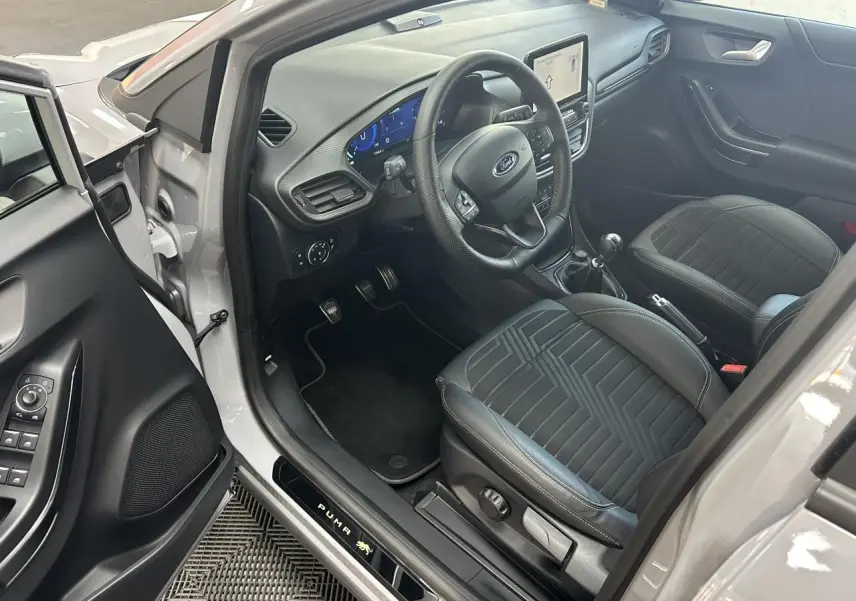 Intérieur côté conducteur du Ford Puma gris 2023, volant multifonction, sièges noirs et écran tactile central visible.