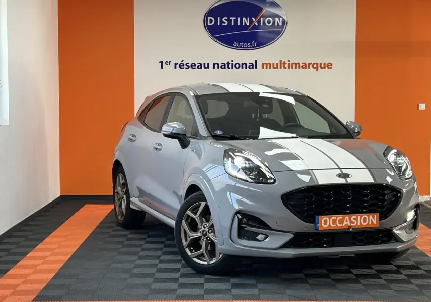 Vue 3/4 avant d'une Ford Puma gris clair avec bandes blanches, jantes alliage et calandre noire dans un showroom.