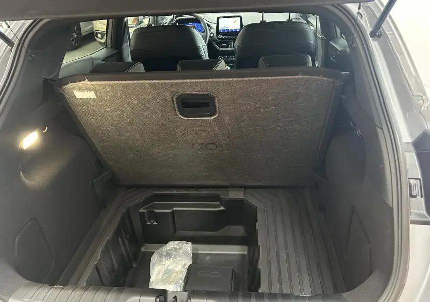 Coffre ouvert vu de l'arrière d'un Ford Puma gris, montrant le compartiment de rangement sous plancher.