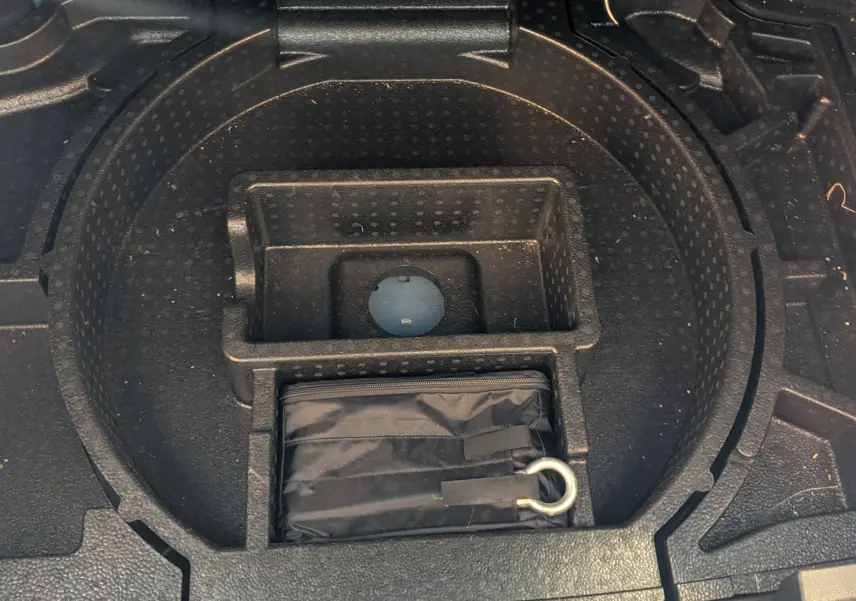 Coffre ouvert d'une Opel Astra bleu 2022, vue sur le rangement sous le plancher avec kit de secours noir.