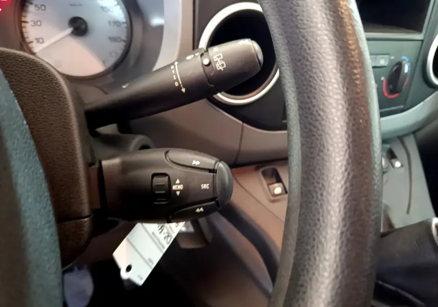 Gros plan sur la colonne de direction et commandes au volant du Citroën Berlingo rouge, tableau de bord en arrière-plan.