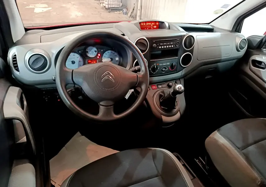 Vue intérieure avant du Citroën Berlingo rouge 2016, volant, tableau de bord et levier de vitesse manuelle visibles.
