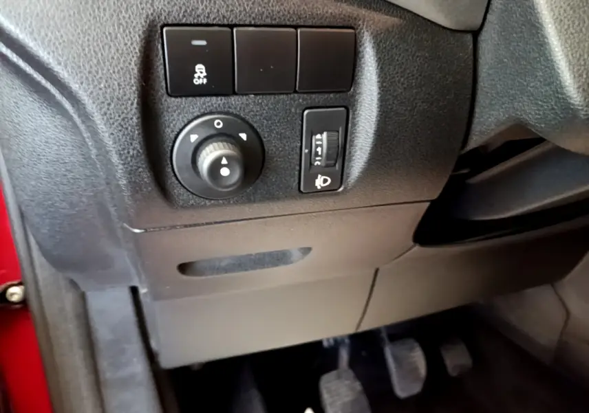 Détail intérieur côté gauche du tableau de bord noir avec commandes de réglage des phares et antipatinage sur Citroën Berlingo rouge.