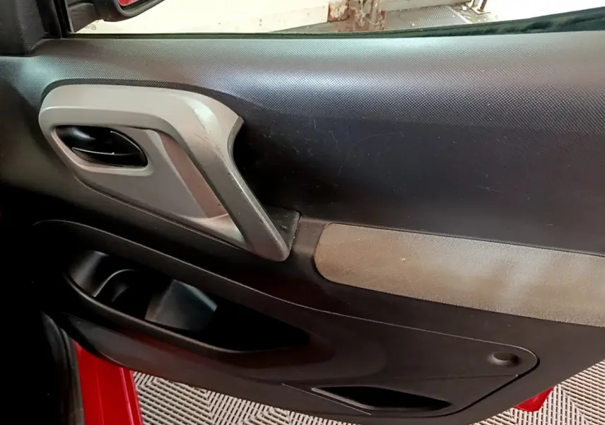 Détail de la porte intérieure côté conducteur du Citroën Berlingo rouge 2016 avec poignée grise et accoudoir noir.