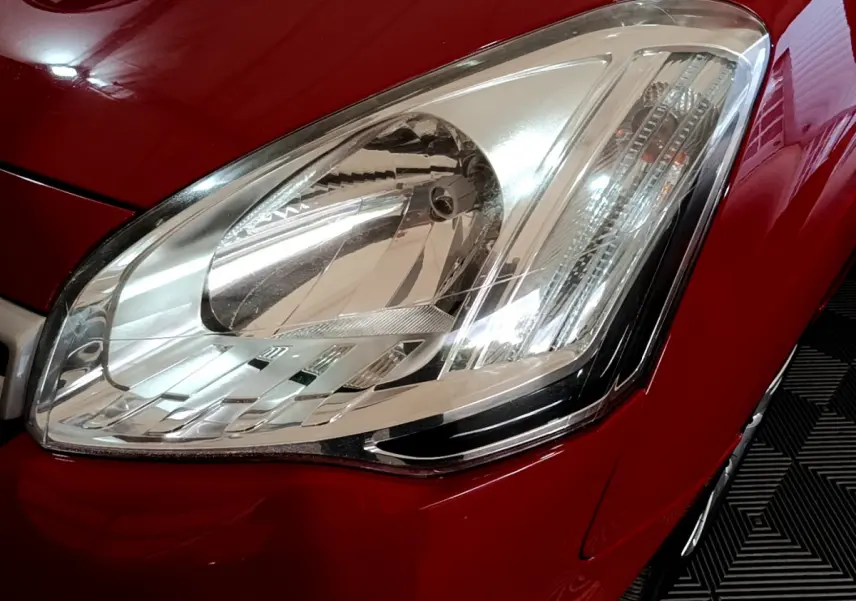 Gros plan sur le phare avant droit d'un Citroën Berlingo rouge 2016, mettant en valeur la finition lumineuse détaillée.
