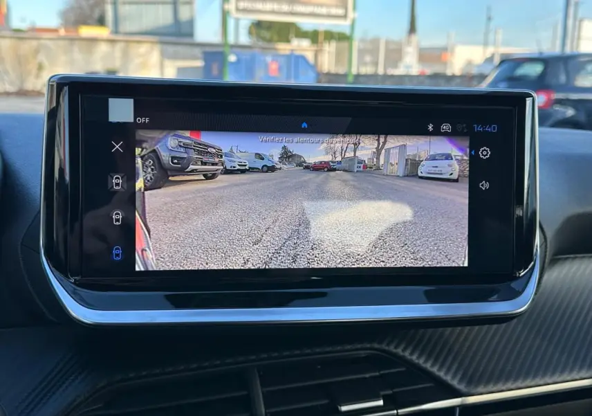 Écran tactile du cockpit numérique montrant la caméra de recul avec vue sur un parking extérieur.