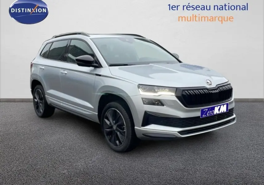 Vue 3/4 avant d'un Skoda Karoq argent 2025 avec barres de toit et jantes noires, sur fond neutre intérieur.