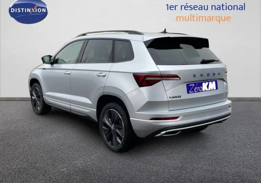 Vue 3/4 arrière droite d'un Skoda Karoq argent 2025 avec barres de toit et vitres teintées.
