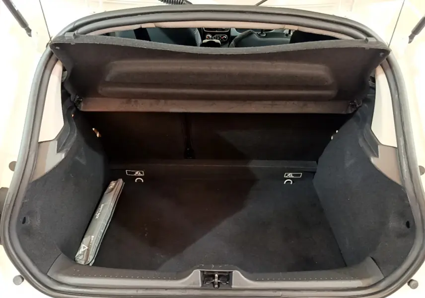Coffre ouvert vu de dessus d'une Renault Clio blanche, montrant un espace de rangement noir et une trousse de secours.