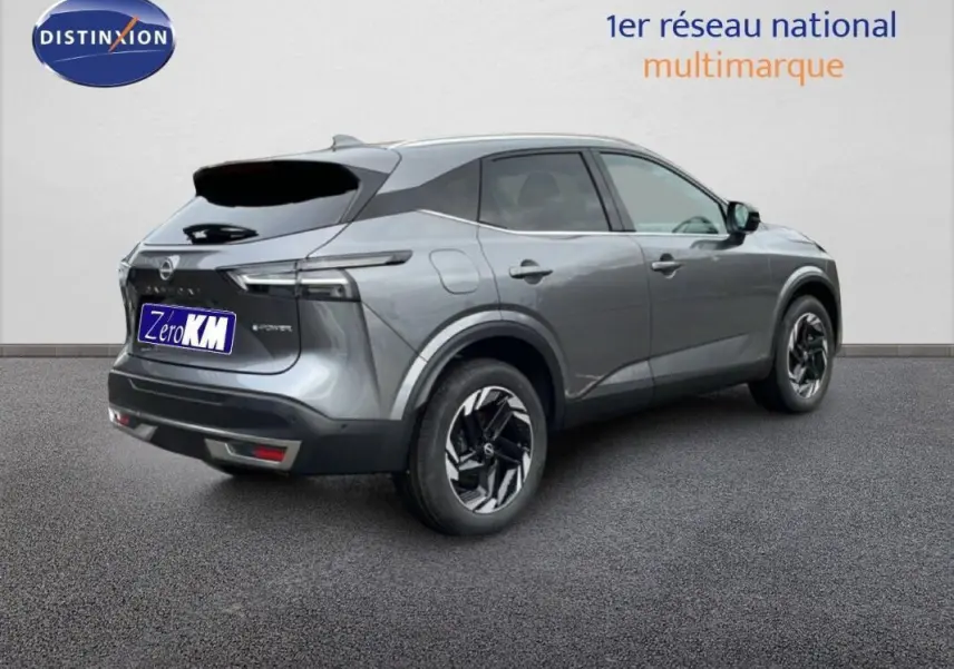Vue 3/4 arrière droite du Nissan Qashqai gris 2025 avec barres de toit et jantes noires distinctives.