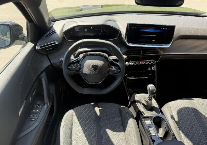Vue intérieure avant du Peugeot 2008 2025 noir perla, volant compact, tableau de bord numérique et levier de vitesse manuel visible.