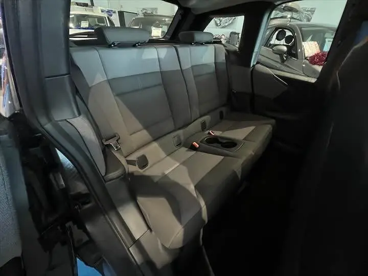 Vue intérieure arrière de la BMW i3 noire, montrant les sièges arrière en tissu gris bleu avec accoudoir central.