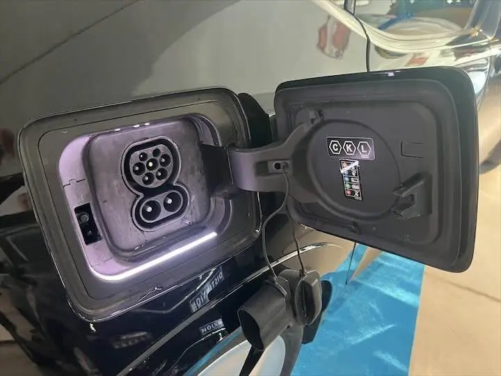 Prise de recharge ouverte côté gauche d'une BMW i3 noire, mettant en valeur le port électrique et le câble débranché.