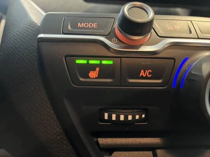 Gros plan sur les commandes de chauffage et climatisation du tableau de bord de la BMW i3 noire, avec témoin vert allumé.