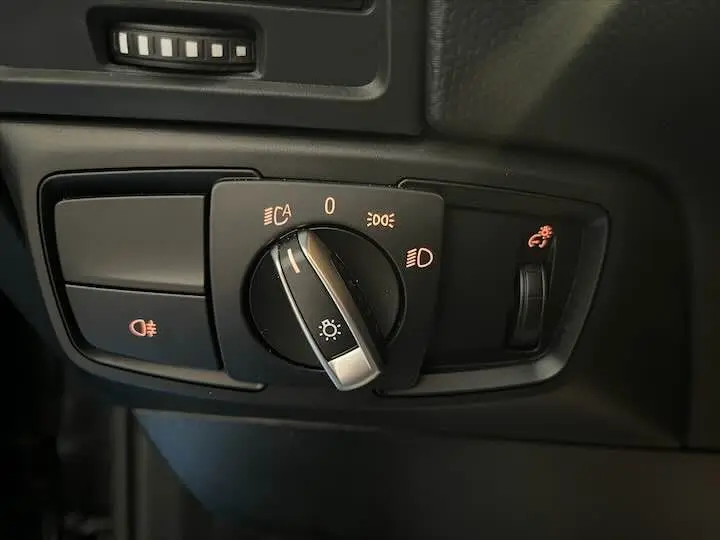 Gros plan sur le bouton de commande des phares et réglage de luminosité intérieur d'une BMW i3 noire de 2022.