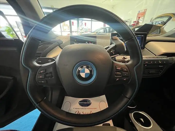 Vue centrée sur le volant noir de la BMW i3 électrique 2022, avec tableau de bord et écran multimédia en arrière-plan.