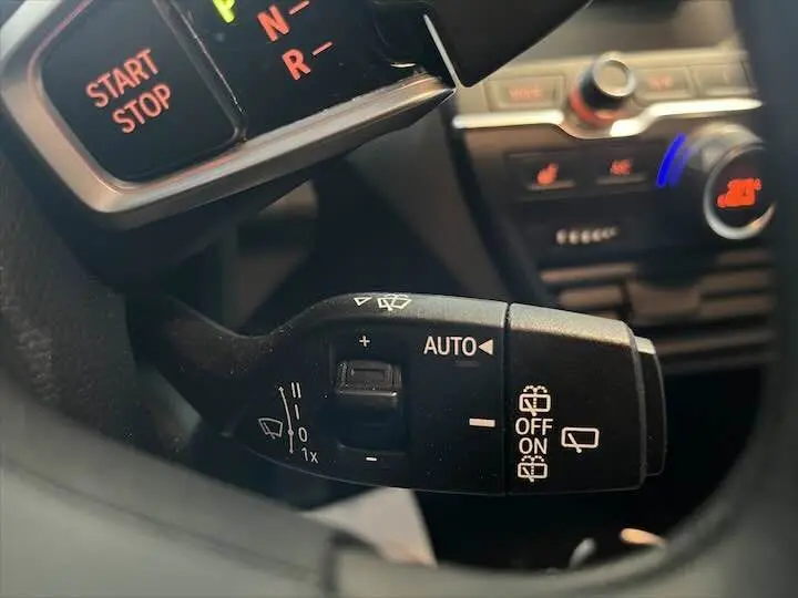 Gros plan sur la commande d'essuie-glace automatique du BMW i3 noir, avec tableau de bord et climatisation en arrière-plan.