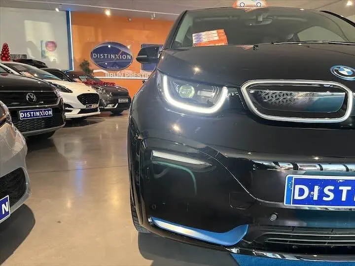 Vue avant rapprochée d'une BMW i3 noire avec phares LED allumés dans un showroom lumineux.