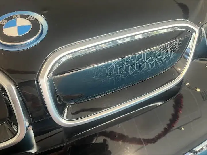 Gros plan sur la calandre fermée noire et chromée d'une BMW i3 électrique noire avec logo BMW visible.