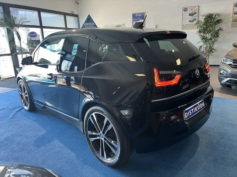BMW i3 noire vue en 3/4 arrière droit dans un showroom, avec feux arrière allumés et jantes sport noires.