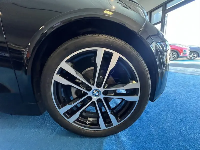 Gros plan sur la roue avant droite noire d'une BMW i3 Edition Windmill avec jante bi-ton élégante en intérieur showroom.