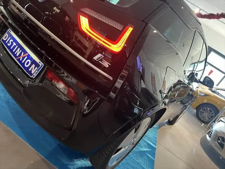 Vue 3/4 arrière droite d'une BMW i3 noire avec feux arrière LED allumés en concession.