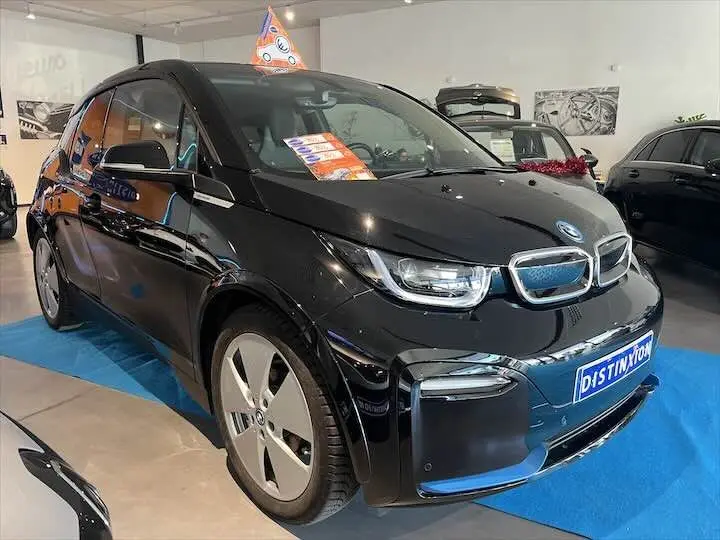 BMW i3 noire vue en 3/4 avant droit dans un showroom, mettant en valeur ses jantes spécifiques et son design compact.
