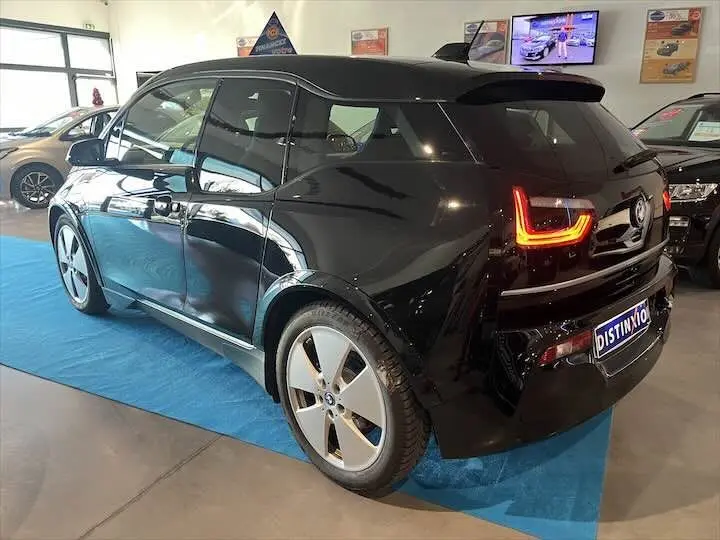 BMW i3 noire vue en 3/4 arrière droit, avec feux arrière LED allumés dans un showroom lumineux.