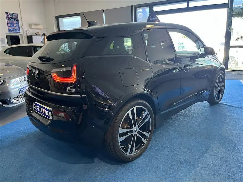 BMW i3 noire vue en 3/4 arrière droit dans un showroom, avec feux arrière LED allumés et jantes bicolores.