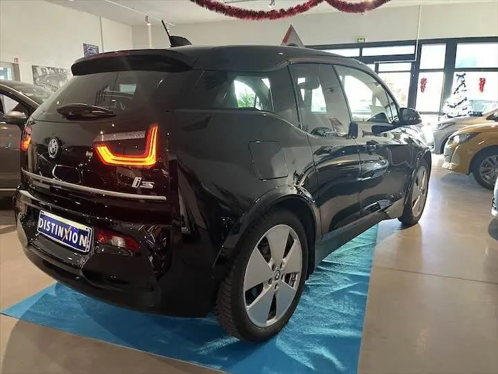 Vue 3/4 arrière droite d'une BMW i3 S noire avec feux arrière LED allumés en showroom.