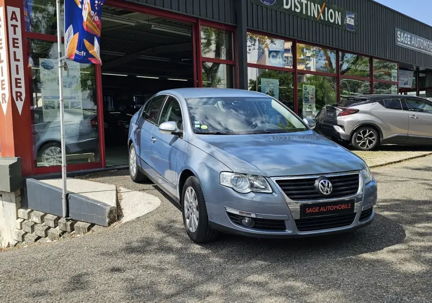 Volkswagen Passat 1.4 TSI bleu vue 3/4 avant droit devant un garage avec plaque Sage Automobile.