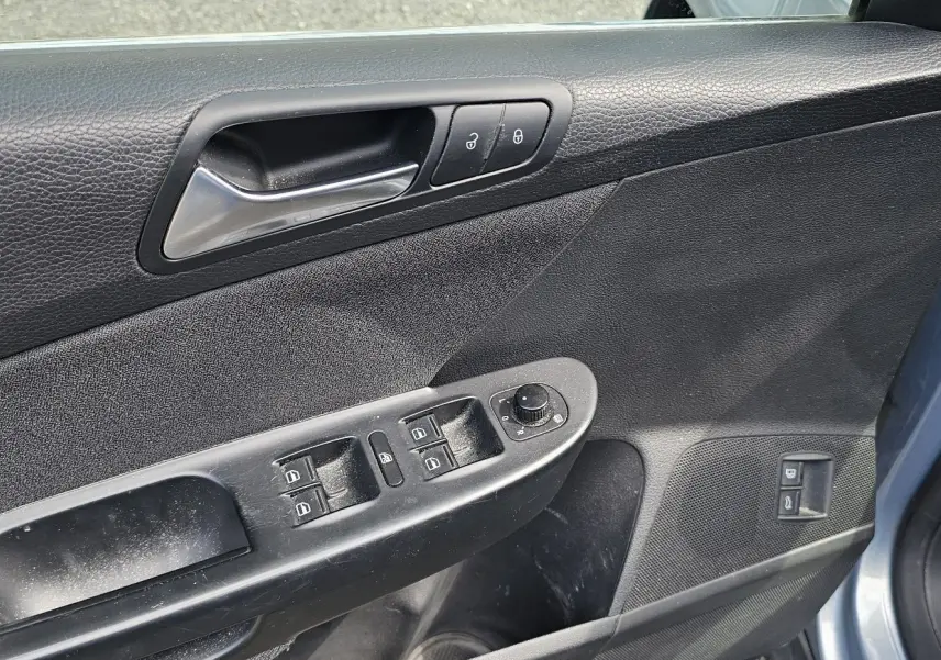 Vue rapprochée de la portière avant gauche bleue d'une Volkswagen Passat 2009, avec commandes électriques et poignée chrome.