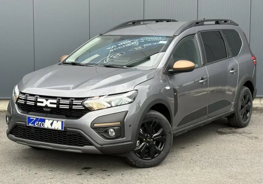 Dacia Jogger Gris Schiste en 3/4 avant droit avec jantes noires et coques de rétroviseurs couleur cuivre.
